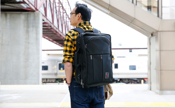 A person carrying a Black 525 Ballistic Western Flyer via the included backpack straps at a rail station.